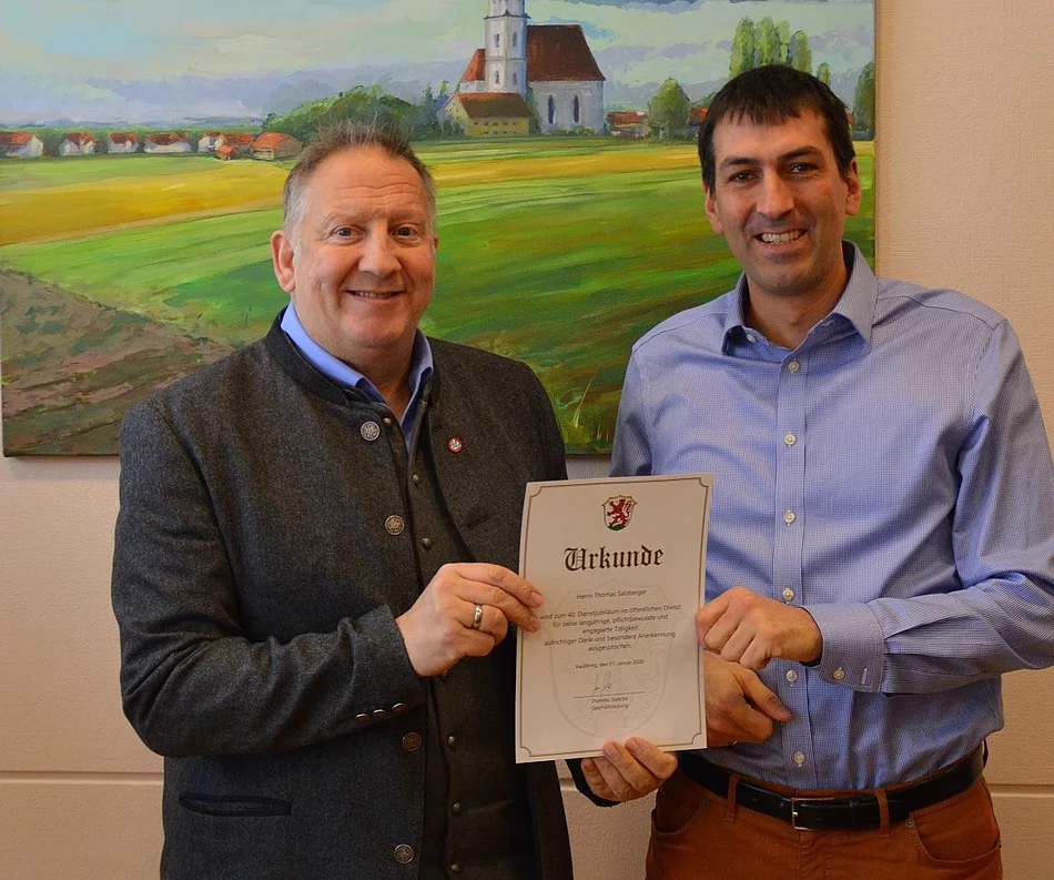 Zwei Männer stehen vor einem Gemälde einer Kirche in einer Landschaft und halten gemeinsam eine Urkunde