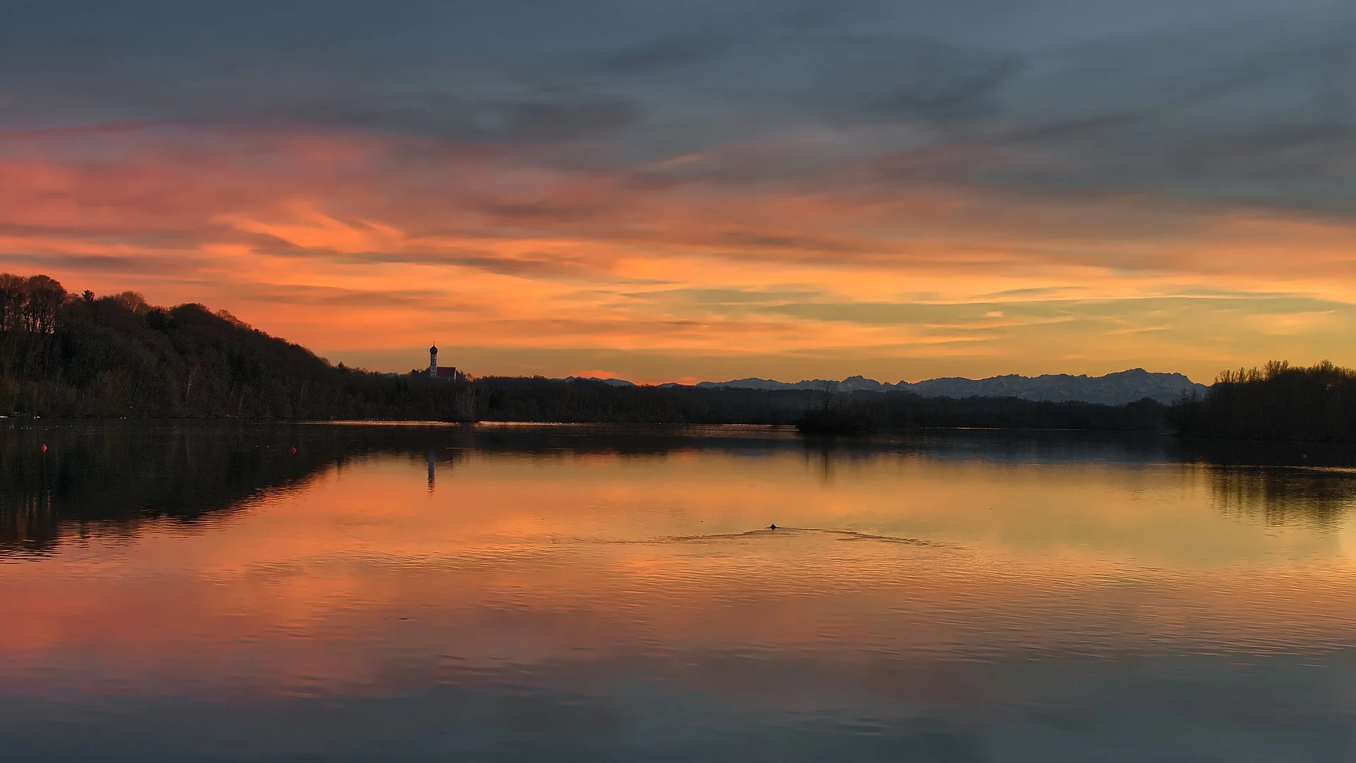 Stausee Kaufering im Abendrot. Hinten am Horzont sieht man die Pfarrkirche St. Johann von Alt-Kaufering.