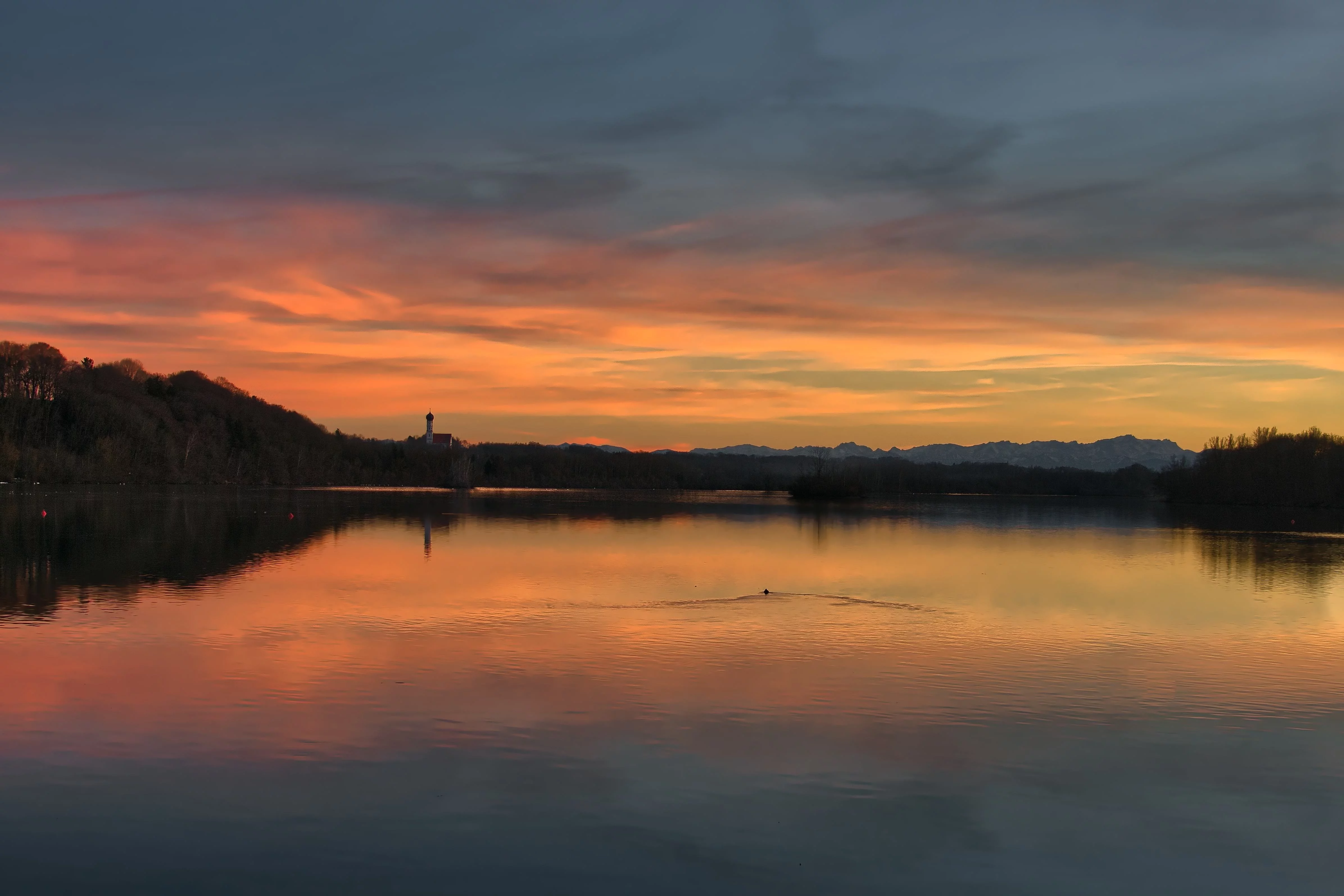 Stausee Kaufering im Abendrot. Hinten am Horzont sieht man die Pfarrkirche St. Johann von Alt-Kaufering.