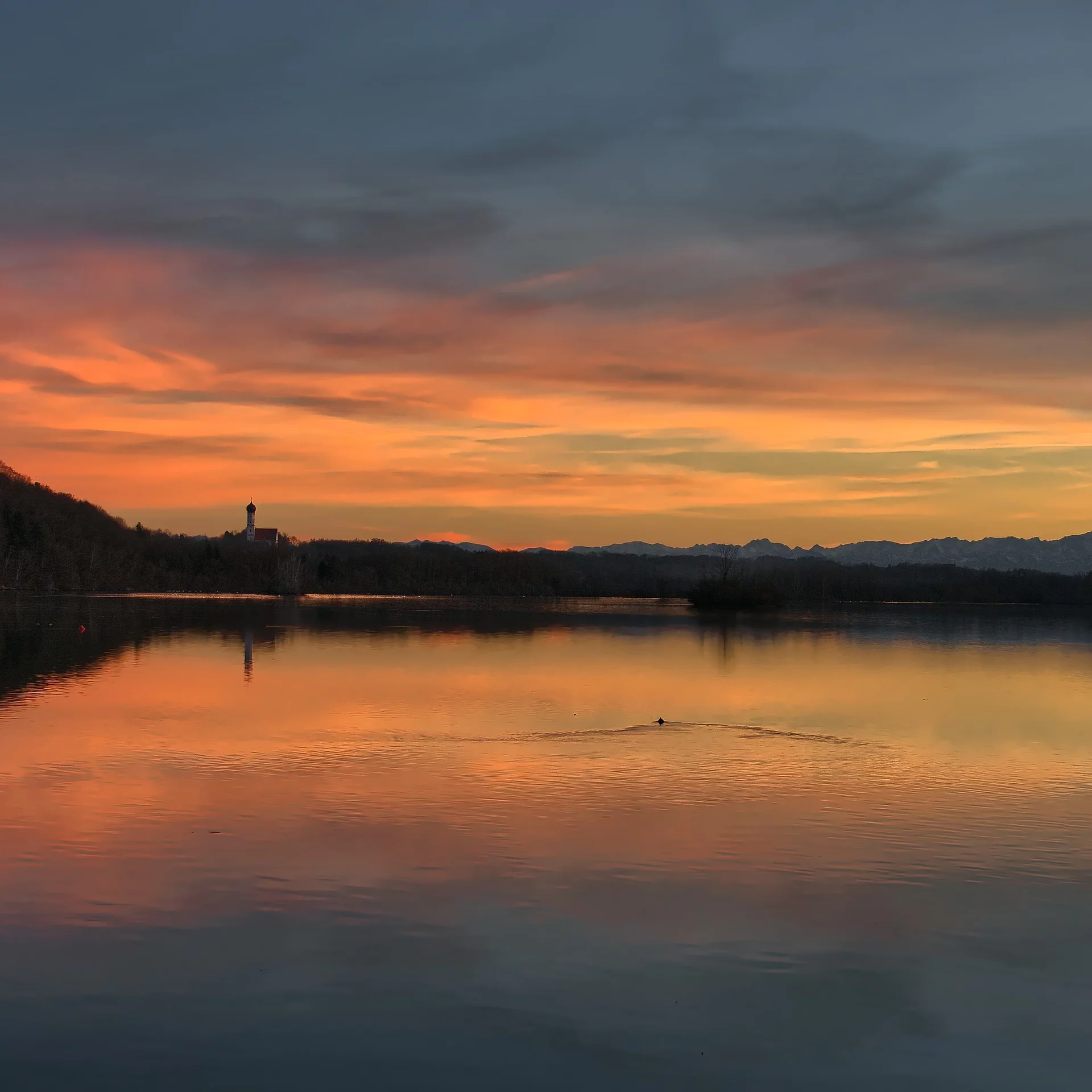 Stausee Kaufering im Abendrot. Hinten am Horzont sieht man die Pfarrkirche St. Johann von Alt-Kaufering.