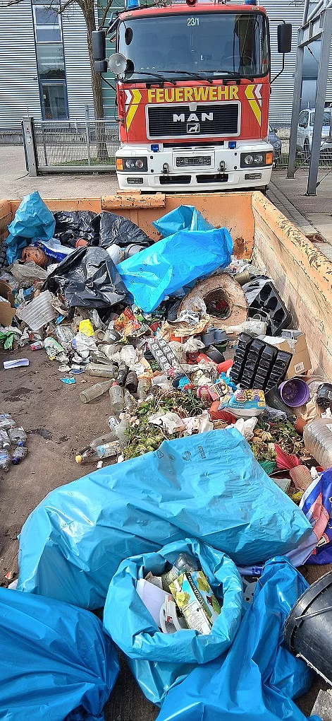 Müllsammlung von Aktion Saubere Landschaft 2026 in Kaufering. Im Hintergrund steht ein Feuerwehrauto. Vorne Müllcontainer mit blauen Müllsäcken voll mit Müll.