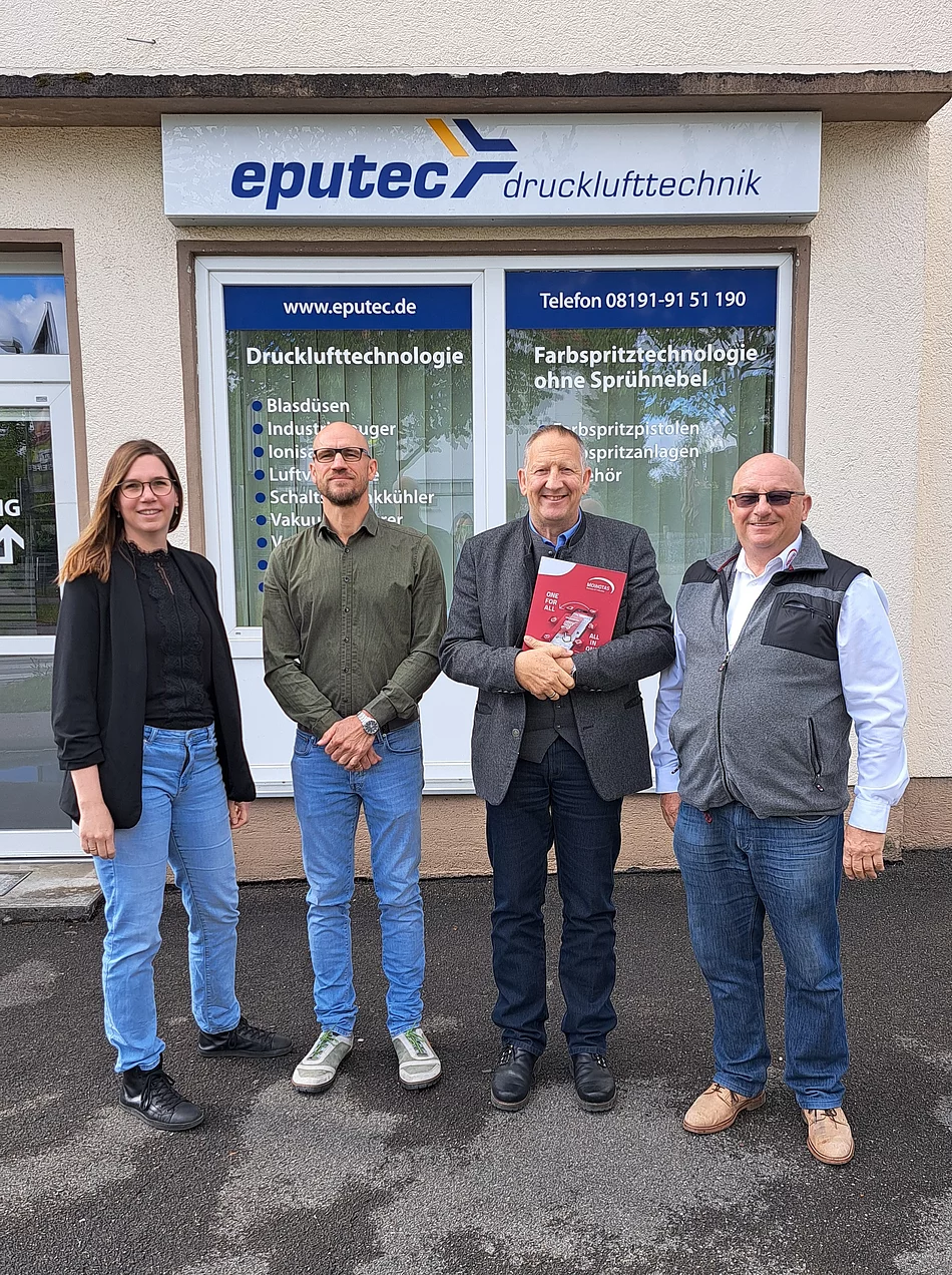 Vier Personen stehen vor einem Gebäude mit Schildern der Firma eputec Drucklufttechnik