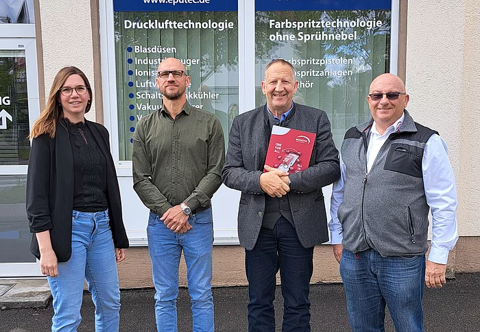Vier Personen stehen vor einem Gebäude mit Schildern der Firma eputec Drucklufttechnik