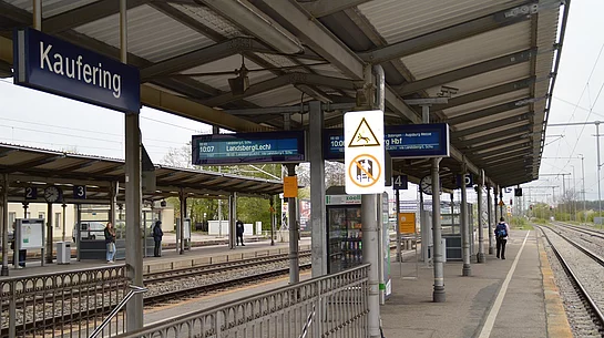 Bahnsteig mit Überdachung, Fahrgastinformationsanzeigen und Schild mit dem Stationsnamen Kaufering